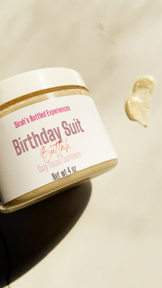 Jar of 'Birthday Suit' body butter with a white label on a beige background