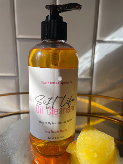 Bottle of 'Soft Life' skin cleanser with a pump and a pineapple on a tiled surface.
