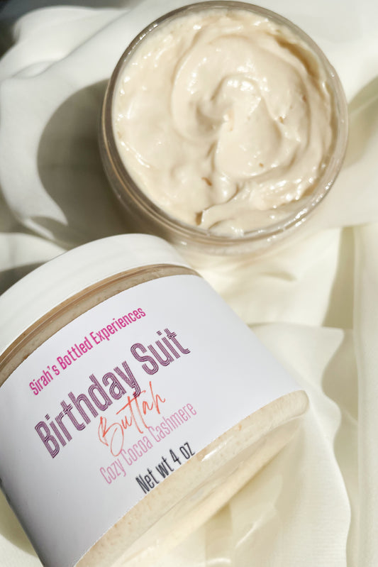 Jar of 'Birthday Suit Buttah' shea butters on a white fabric background
