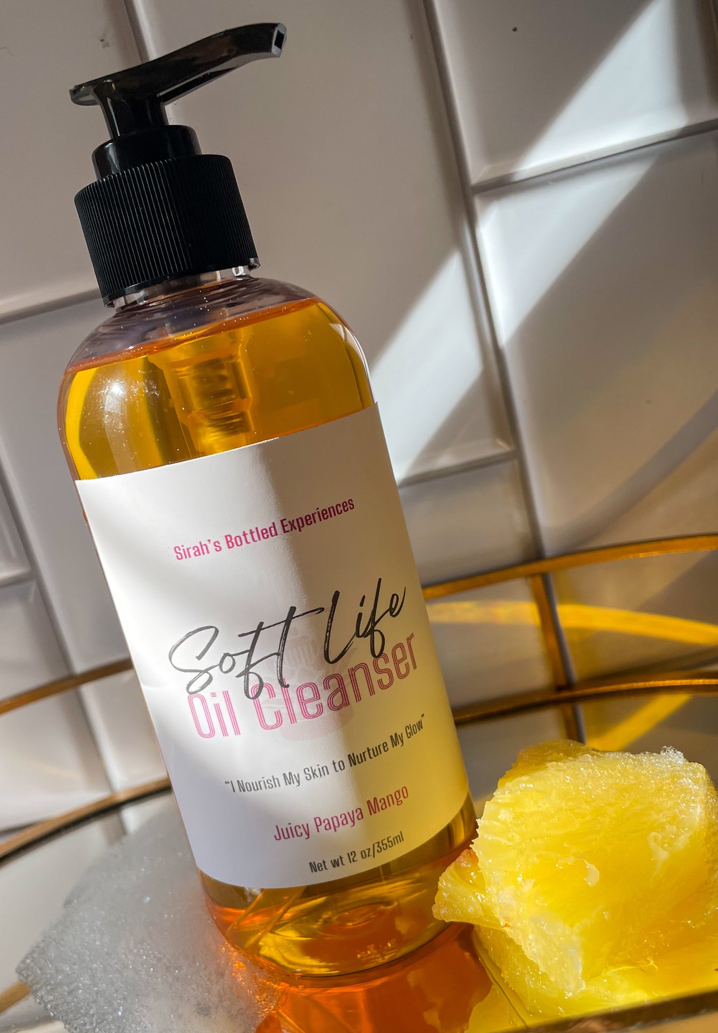 Bottle of 'Soft Life Oil Cleanser' with a pump on a tiled bathroom floor.