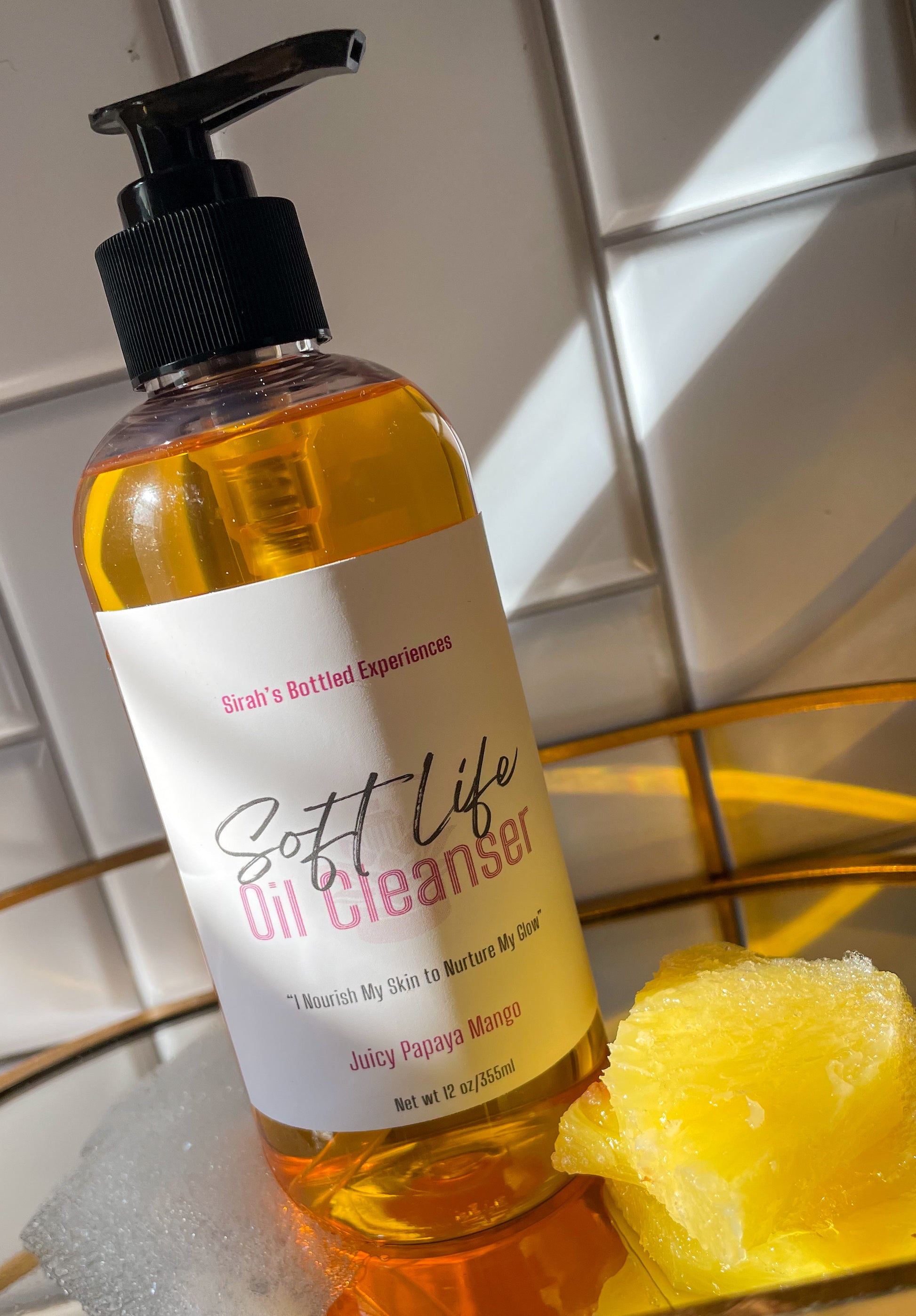 Bottle of 'Soft Life Oil Cleanser' with a pump on a tiled bathroom floor.