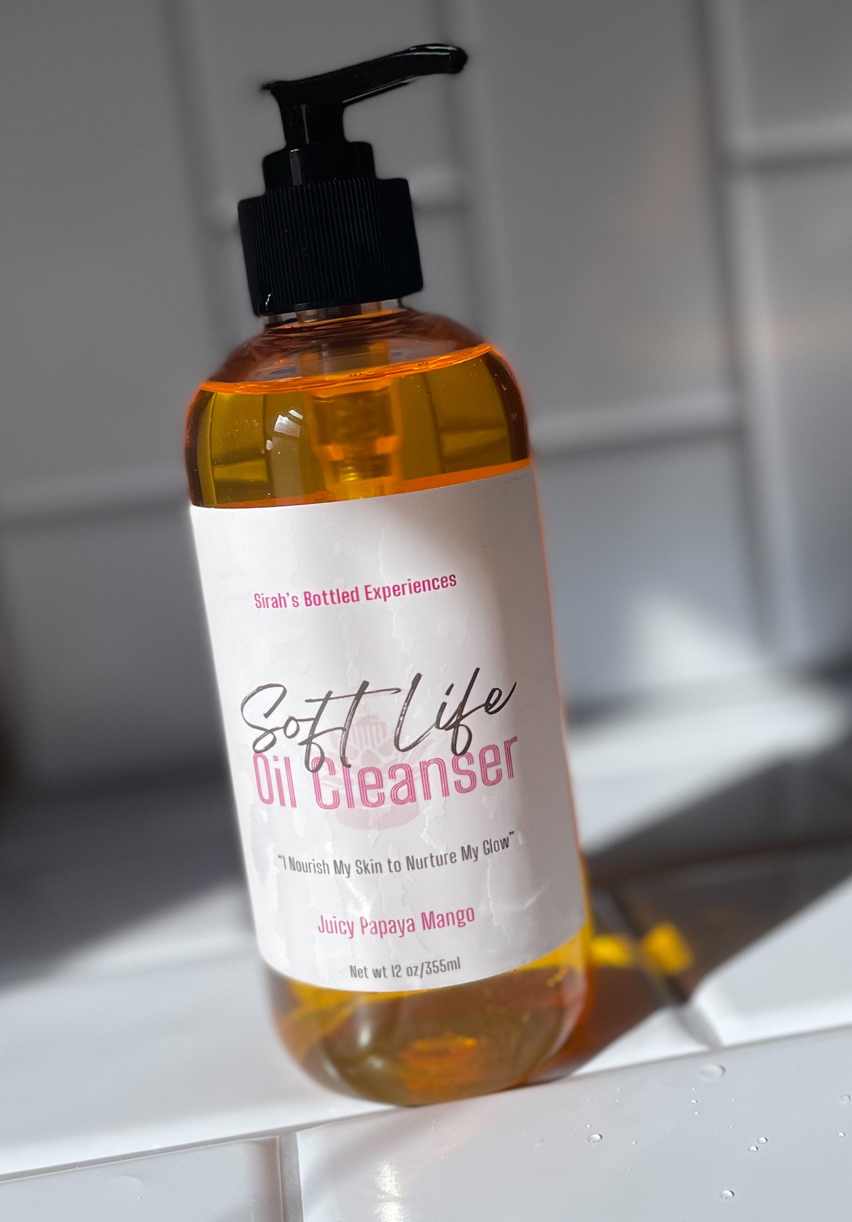 Bottle of 'Soft Life Oil Cleanser' on a white surface with a blurred background