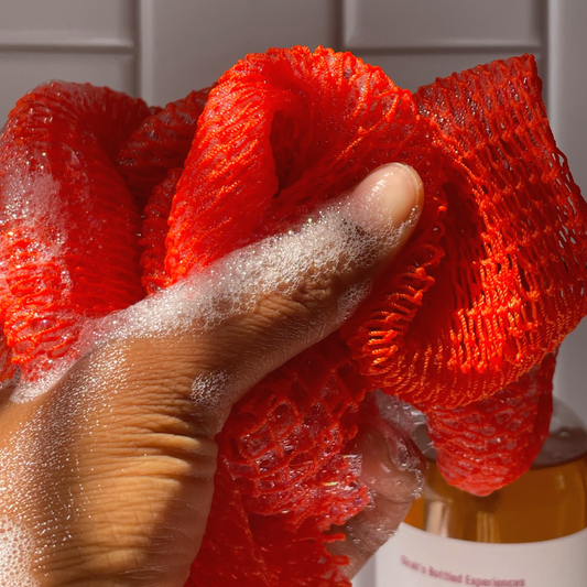 Hand holding an African net sponge with soap suds against a neutral background
